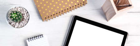 Panoramic top view on a wooden desk with a tablet, cactus, a notebook and spiral notebook with...