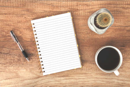 Top view on a wooden desk with open notebook, coffee cup and cactus