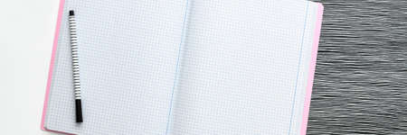 Blank notebook is open on modern white working table. Top view. Mockup with pastel pink elements. Black and white concept. Minimal panoramic compositionの写真素材