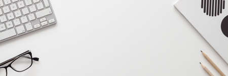 White office desk with copy space. Keyboard, notebook, glasses, pencils. View from above. Panoramaの写真素材