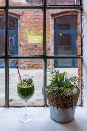 An industrial window overlooking an old red brick factory. Window sill with flower and green healthy cocktailの写真素材