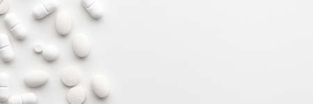 Scattered white pills on a white background. Bright monochrome composition. Pharmacology. Copy space. Panoramaの写真素材