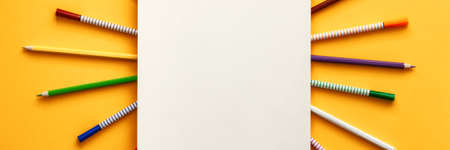 Yellow background with an empty sketchbook as a mockup. Colorful pencils and markers scattered around. Concept desk. Panoramic top view.の写真素材