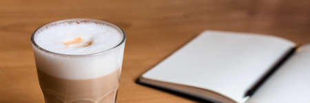 Wooden table with latte coffee and an open notebook for notes. Panoramic photoの写真素材