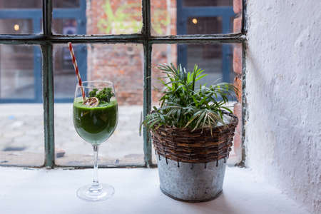 An industrial window overlooking an old red brick factory. White window sill with flower and green healthy cocktail. Copy spaceの写真素材