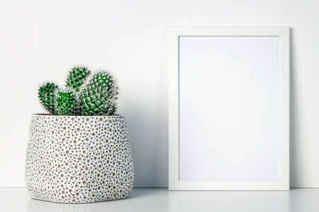 White shelf in the house with a cactus in a pot with a dot pattern and a white frame mockup. Hipster decoration. Scandinavian style. A place for your text or graphics.の写真素材