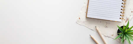White office desk with copy space. Open notebook, pencils, handmade paper and succulent. View from above. Panoramic photoの写真素材