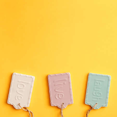 A blank yellow background with space for text. Copy space. Ceramic decorations with the letters laugh, live and love. Pastel colors. Concept composition. Top view, minimalの写真素材