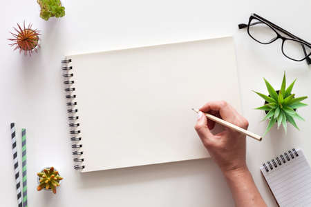 A white desk with an open sketchbook and a woman's hand. Drawing. View from above. Creative desk. Mockup.の写真素材
