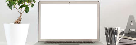 A business desk against a gray wall with an open laptop. Mockup screen. Panorama.の写真素材