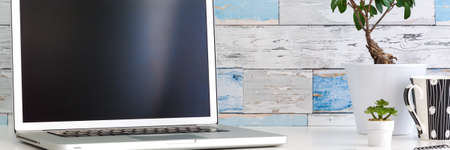Home office desk with an open laptop. Screen mockup. A wall with old boards. Office items. A plant in a pot. Panorama.の写真素材