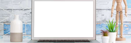 Desk with an open laptop and office supplies. Screen mockup. Wooden puppet. Geometric toolbox. A wall of old wooden boards. Panorama.の写真素材