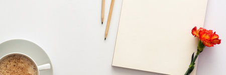 White table at home. Open empty sketchbook, wooden pencils and an orange-red carnation. Cocoa with foam in a white cup. Mockup. Creative desk. Panoramaの写真素材