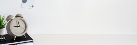 School desk against an empty white wall. Copy space. Books, succulent and alarm clock.Sticky note. Panoramaの写真素材