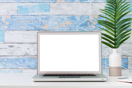 An open laptop on a white desk. Mockup. A palm tree in a vase. A wall made of old blue boards.の写真素材