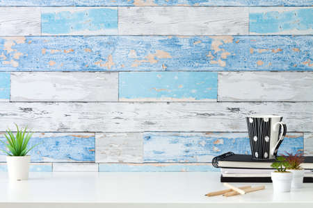 Succulent plant in a white pot and a cup with coffee and office supplies. A wall made of old blue boards. Copy spaceの写真素材