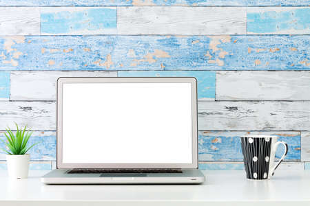 An open laptop on a white desk. Mockup. Succulent plant in a white pot and a cup of coffee. A wall made of old blue boards.の写真素材