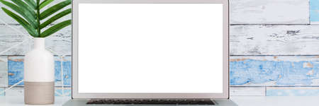 An open laptop on a white desk. Mockup. A palm tree in a vase. A wall made of old blue boards. Bannerの写真素材