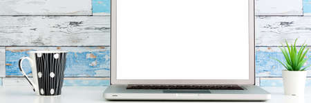 An open laptop on a white desk. Mockup. Succulent plant in a white pot and a cup of coffee. A wall made of old blue boards. Bannerの写真素材