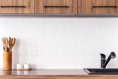 Industrial kitchen. White ceramic tiles as copy space. Black kitchen faucet and wooden furniture.