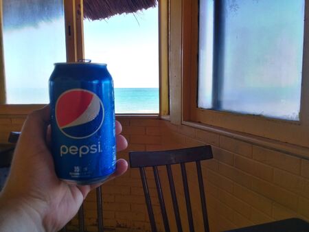 Maceio, AL, Brazil - May 19, 2019 - Hand holding a can of Pepsi and in the background a window overlooking the seaのeditorial素材