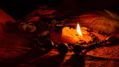 Close-up of a beeswax candle and a seed bead necklace on orange fabric. Low light