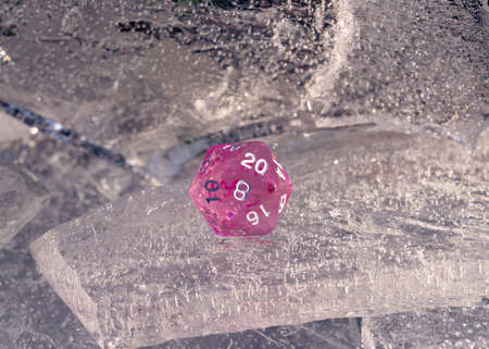 Image of one pink 20 sided role playing die on a sheet of ice in the winter's sunの写真素材