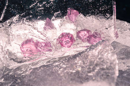 Image of a set of rpg dice behind a sheet of ice in the sun light. Focused on the 20 sided die and the sheet of iceの写真素材