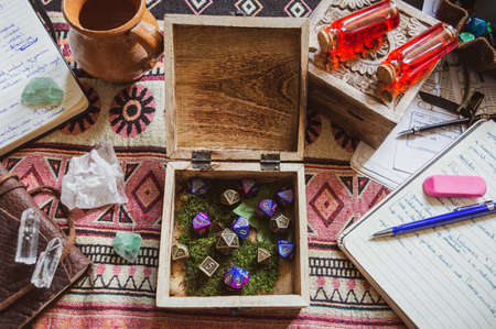 An image of an open wooden box with metallic and plastic purple role-playing dice surrounded by notebooks, crystals and pen and paper on a textured plaidの写真素材