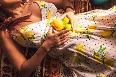 Indonesian woman wearing a white dress with lemons and polka dots laying on a colorful couch holding...