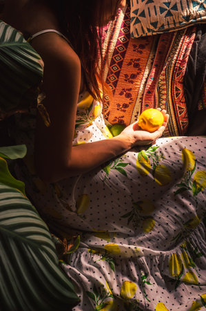 Indonesian woman wearing a white dress with lemons and polka dots sitting on the ground holding a lemon - vertical imageの写真素材
