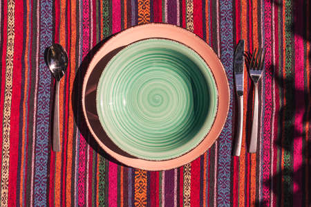 Overhead view image of a plate and soup plate with cutlery on a colorful striped tablecloth in the...