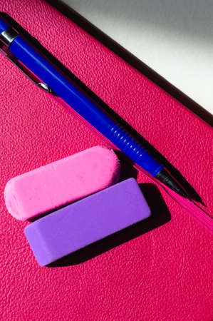 Vertical image of a pink and purple eraser and a blue fill pencil on a pink notebookの写真素材