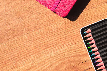 Overhead image of a pink notebook and a tray of colored pencils on a wooden surface