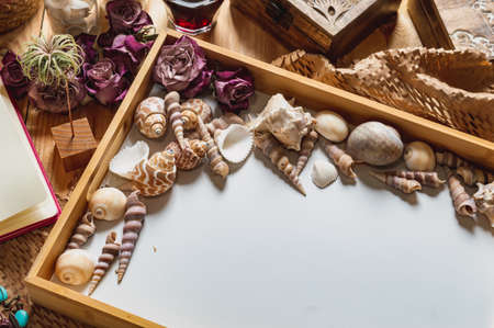 Image of a wooden tray with seashells and dried pink roses on a wooden table