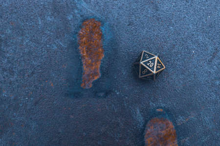 Close-up image of one 20-sided metallic role-playing die on a rusty surface in cool light.