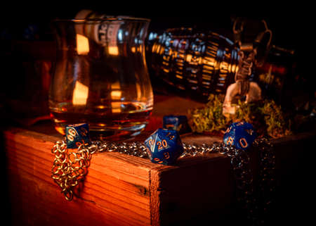 Close-up image of a blue d20 on a wooden box within the background a whiskey glass and glass bottleの写真素材