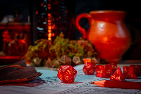 Close-up image of a red 20-sided role-playing gaming die within the background a set of dice and ceramic jarの写真素材