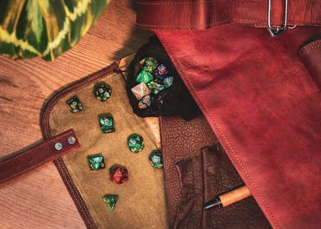 Overhead image of an open brown leather messenger bag containing a dice bag with roleplaying dice and a leather notebook and a penの写真素材