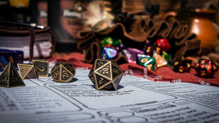Low angle image of a brass 20-sided die on a character sheet in the sun. In the background are a dice bag and a notebookの写真素材