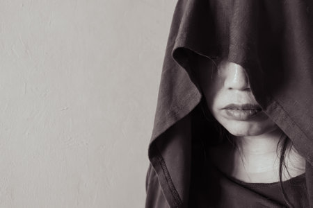 Intense close-up of a woman in a hood, her face partly veiled in shadow, casting a mysterious and contemplative expressionの写真素材