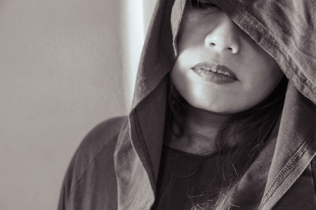 Portrait of a mysterious woman with her face partially concealed by a hood, captured in evocative monochrome, emphasizing texture and mood.の写真素材