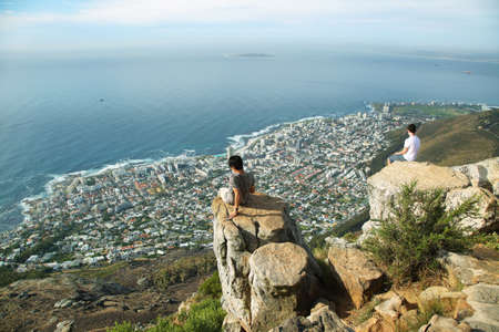 CAPE TOWN, SOUTH AFRICA - DECEMBER 7: Young men looking at view of the cityspace and coast from the edge of Lions Head peak on December 7, 2014 in Cape Town, south Africa.のeditorial素材
