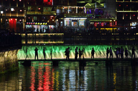 FENGHUANG, CHINA - SEPTEMBER 16, 2015: View of people and illuminated riverside houses in ancient town of Fenghuang known as Phoenix, Chinaのeditorial素材