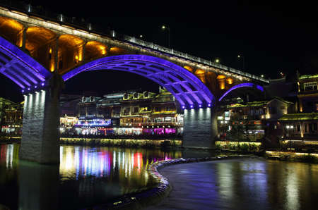 FENGHUANG, CHINA - SEPTEMBER 16, 2015: View of illuminated riverside houses and bridge in ancient town of Fenghuang known as Phoenix, Chinaのeditorial素材