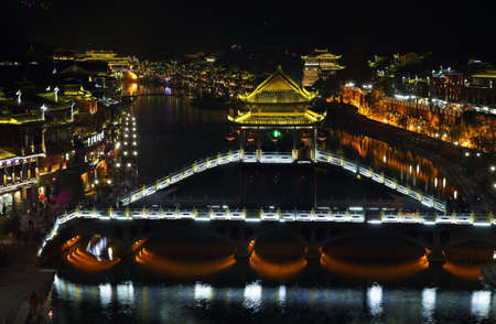 FENGHUANG, CHINA - SEPTEMBER 15, 2015: View of illuminated stone bridge over Tuo Jiang river and wooden houses in ancient town of Fenghuang known as Phoenix, Chinaのeditorial素材