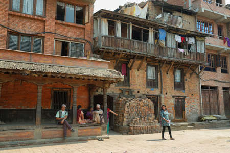 BHAKTAPUR, NEPAL - APRIL 20, 2016: hindu people resting in the shade on a porch of a building in a beautiful street of medieval town of Bhaktapur in Nepal.のeditorial素材