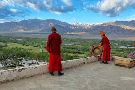 Ladakh, India - September 3, 2019: Two monks calling for the morning prayers from the rooftop of...