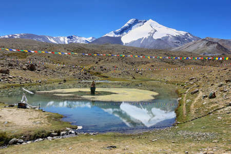 Kang Yatse I and II summits (6496m and 6250m) reflected in a lake with a Buddha statue in the...