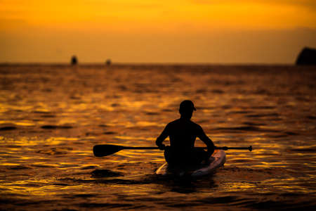 a man rowing a paddle board on the ocean into the Costa Rican sunset